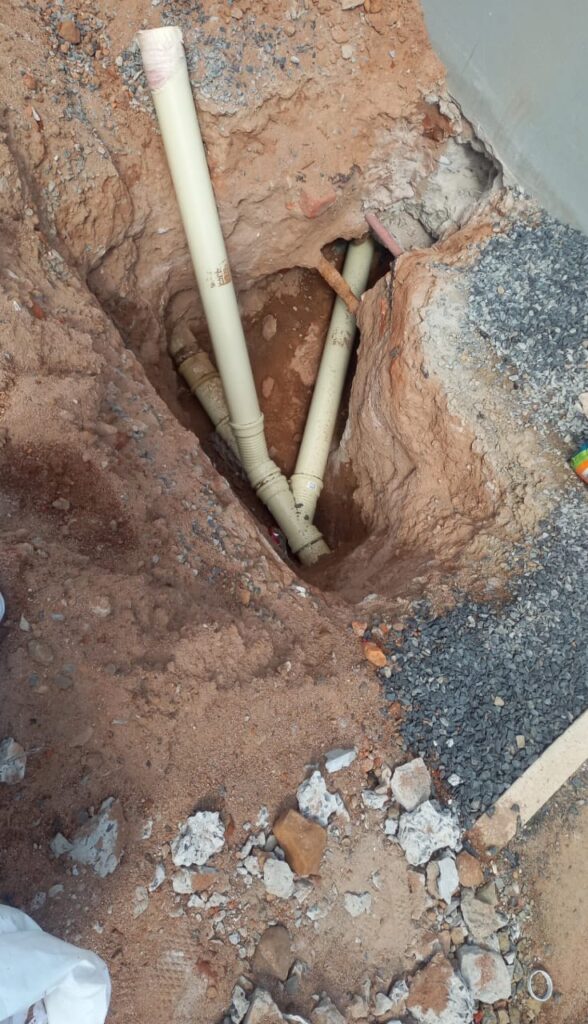 Excavated trench revealing underground PVC plumbing pipes during a residential or commercial water line repair service.