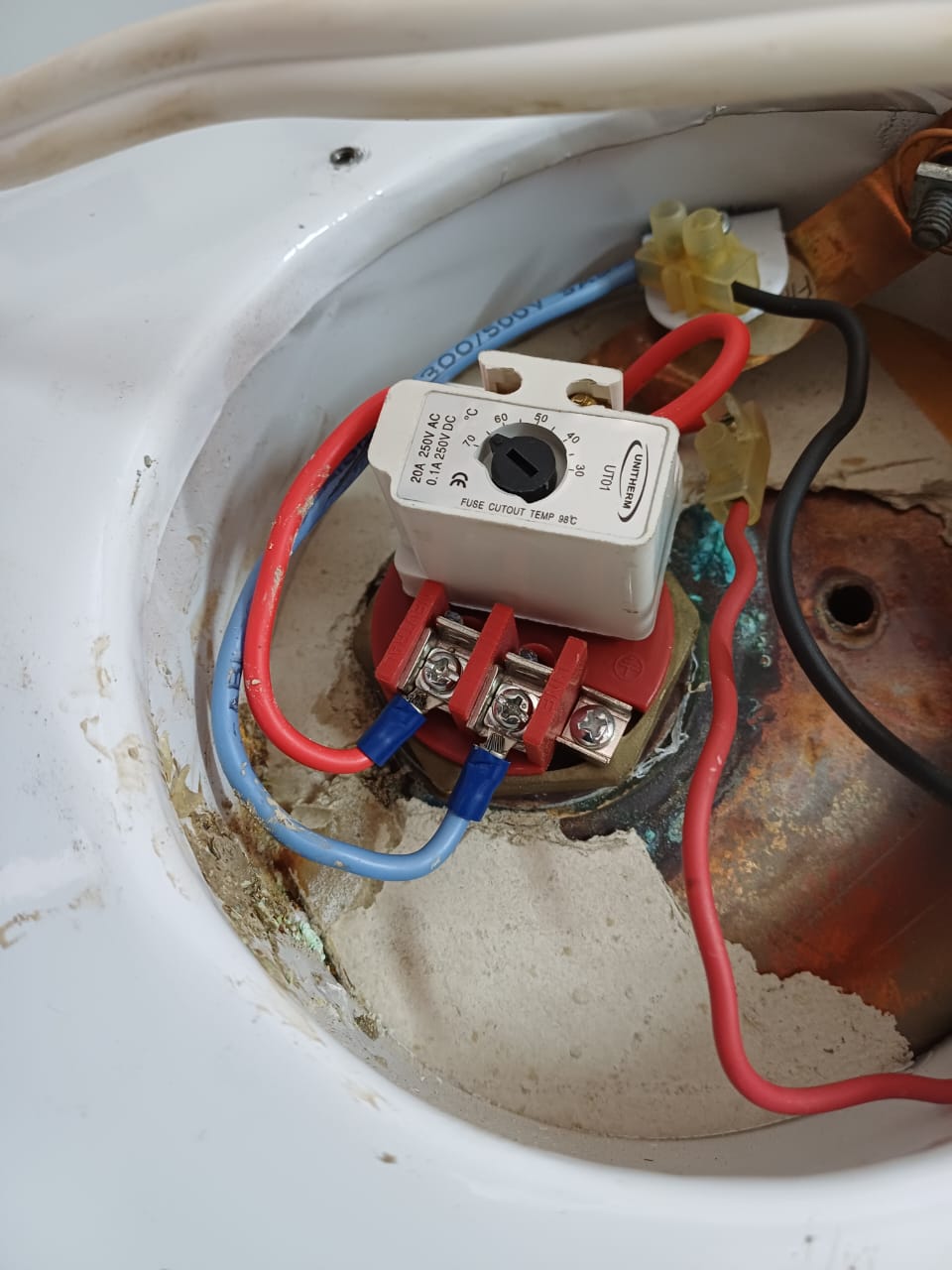 Close-up view of the internal wiring of a water heater showing a newly installed white Uniterm thermostat and heating element base, properly connected with red and blue electrical wires.